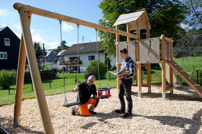 Bild vergr��ern: Der Bauhof der Gemeinde Wilnsdorf hat auf dem Flammersbacher Spielplatz einen neuen Spielturm mit zwei Aufstiegen, einer Rutsche und zwei Schaukeln aufgebaut, heute haben Bautechniker Tobias Abrams (r.) und sein Kollege Markus Ax die Spiellandschaft freigegeben.
